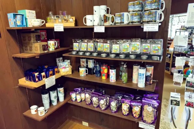 Wooden shelves displaying mugs, tea boxes, and snack bags in a store setting.