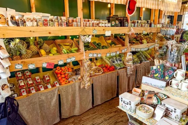 Market stall with fresh fruits, vegetables, and packaged goods on wooden shelves.