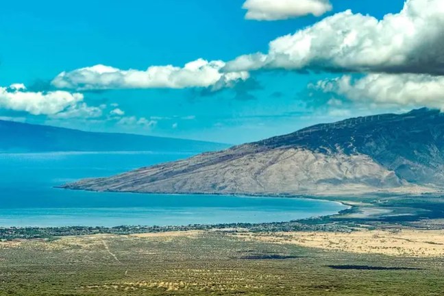 Scenic view of coastline, hills, and ocean under a blue sky with clouds.