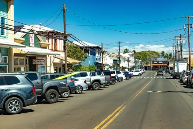 Street view with parked cars and colorful buildings under clear sky.