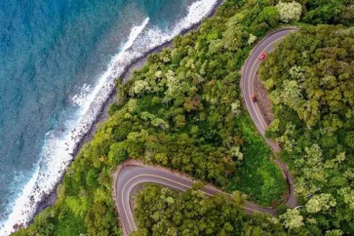 Aerial view of a winding coastal road surrounded by lush greenery and ocean waves.